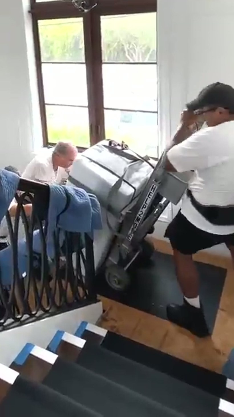 A mover guiding a blanket-wrapped grand piano down a ramp