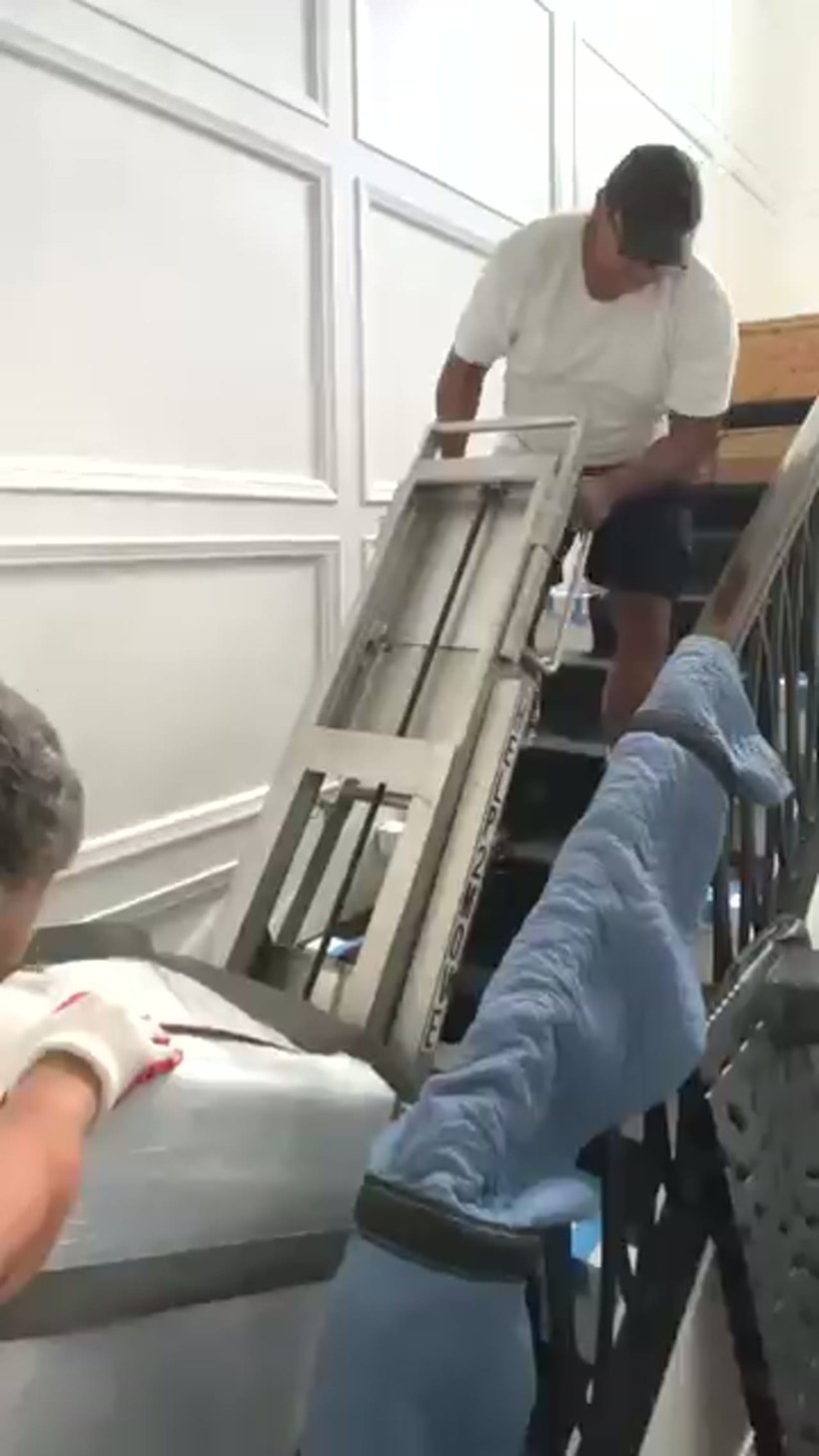 Two movers easing a wrapped safe down a staircase on a stair climber