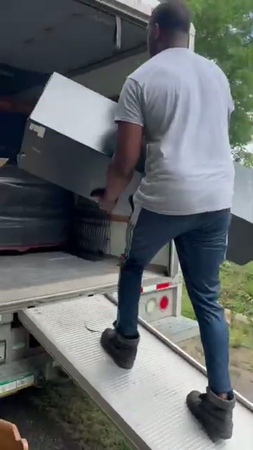 A mover carrying a heavy safe across a yard to the truck